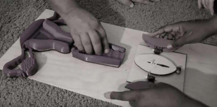 Several hands explore and reposition raised purple anatomy models on a flat teaching board.